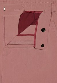 Rosa Stoffhosen verfügen über einen Reißverschluss mit einem burgunderroten Innenfutter, einem metallischen Knopf und kontrastierenden Nähten entlang der Nähte und Taschenränder.