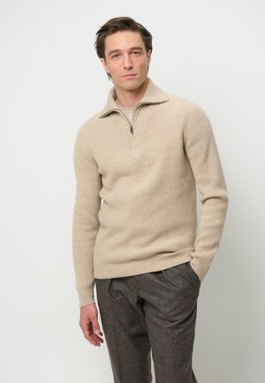 Beige ribbed pullover with a half-zip collar, made from textured knit material. Paired with dark gray tailored trousers.