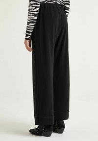 Pantaloni neri a gamba larga con una vestibilità morbida. Caratterizzati da una vita elasticizzata, orlo piegato e abbinati a stivaletti neri con tacco.