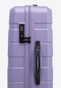 Valise rigide lavande avec une surface texturée, double zip, serrure à combinaison et une poignée noire sur le côté.