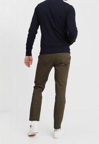 Maglione blu navy e pantaloni verde oliva, caratterizzati da una vestibilità slim, texture liscia e orli risvoltati. Le sneakers bianche completano il look.