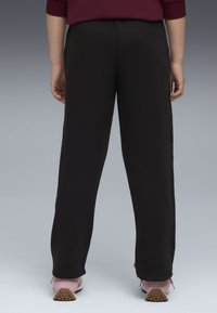 Pantaloni della tuta neri con una vestibilità rilassata, dotati di vita elastica e orli a coste, abbinati a scarpe da ginnastica rosa chiaro.