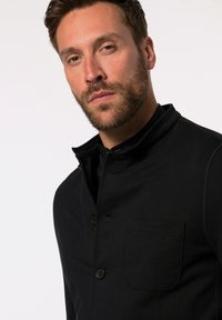 Sort, knaplukket jakke med høj krave, der har en brystlomme og en glat tekstur. Designet til en tætsiddende silhuet.