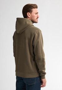 Olivově zelená mikina s kapucí a klokaní kapsou na přední straně, s žebrovanými manžetami a lemem. Materiál vypadá měkký a elastický, s volným střihem.