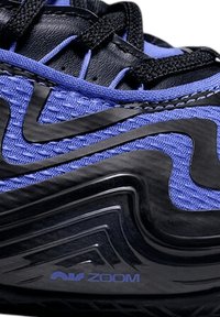 Chaussure de sport noire et violette avec une tige en tissu texturé, des motifs ondulés et un logo "Zoom" bien visible sur la semelle.