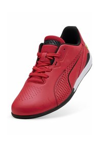 Zapatilla deportiva roja con empeine de cuero liso, acentos de malla, perforaciones para la transpirabilidad, suela negra y detalles en blanco y negro que contrastan.