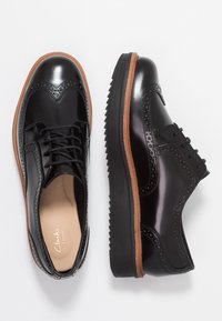 Chaussures brogues en cuir noir à finition lisse, avec des perforations détaillées, un design à lacets et une semelle en caoutchouc contrastée avec un accent marron.