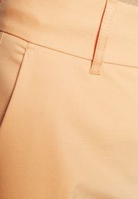 Peach fabric trousers detail featuring a smooth texture, flat front, and neatly stitched waistband with a subtle sheen.
