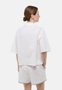 Chemise blanche à manches courtes avec un col et un tissu texturé, assortie à un short blanc avec des coutures noires le long de l'ourlet.