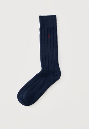Marineblaue, gerippte Socke mit kleinem, rotem, besticktem Logo nahe der Spitze auf einem schlichten, hellen Hintergrund.