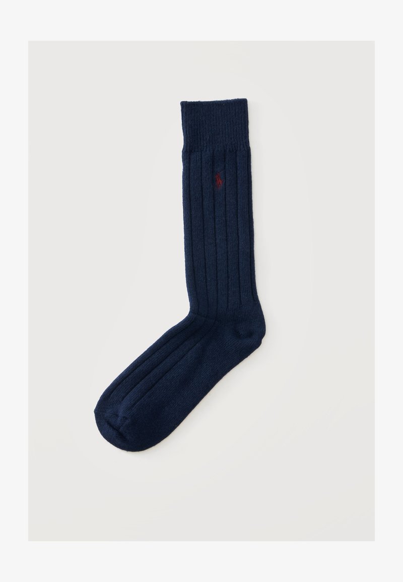 Chaussette côtelée bleu marine avec un petit logo rouge brodé près du haut sur un fond clair uni.