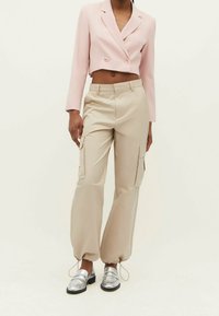 Różowy, krótki żakiet z podwójnymi guzikami, beżowe spodnie bojówki z bocznymi kieszeniami oraz metaliczne srebrne mokasyny z zaokrąglonym noskiem.