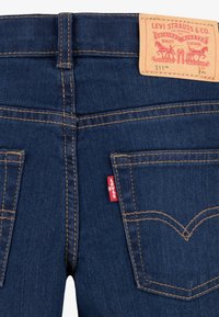 Tummansiniset farkut, joissa näkyvät tikkaukset, kaksi takataskua ja ruskean nahkainen Levi's-logo- ja tuote-erittelylabeli.