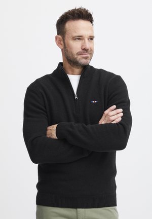 Pull à col zippé noir en tissu doux, avec un petit logo multicolore sur la poitrine et des poignets et un ourlet côtelés.