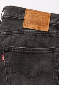 Jean en denim noir avec patch en cuir Levi Strauss indiquant la taille W32 L32 et étiquette en tissu rouge Levi's sur la poche arrière.