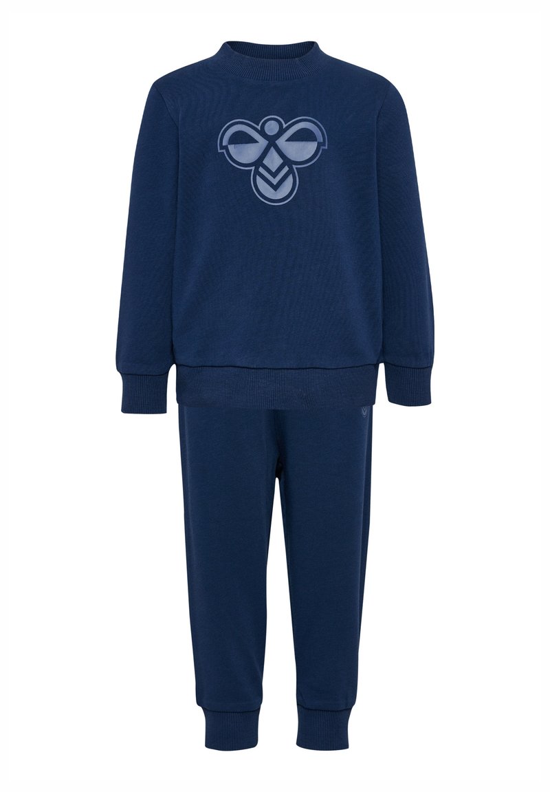 Granatowy dres składający się z dwóch części, wykonany z miękkiego materiału. Bluzka z okrągłym dekoltem zdobiona jest logo, a do niej dopasowane są zwężające się spodnie.