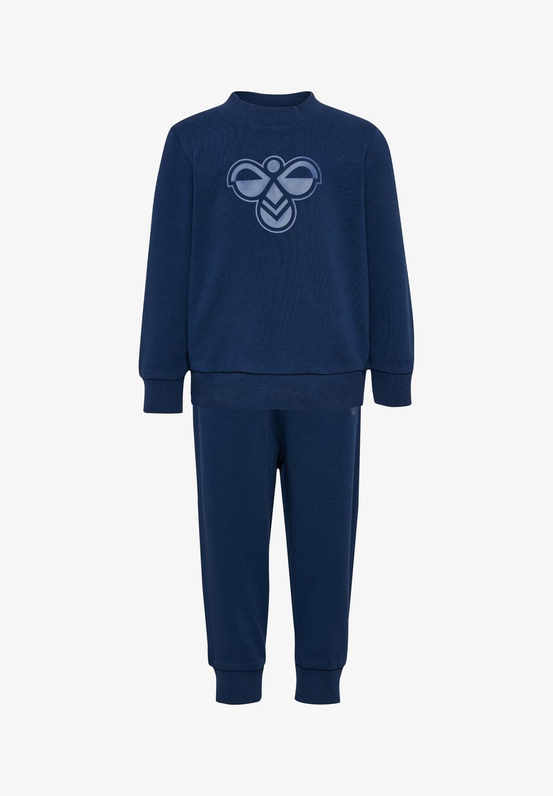 Granatowy dres składający się z dwóch części, wykonany z miękkiego materiału. Bluzka z okrągłym dekoltem zdobiona jest logo, a do niej dopasowane są zwężające się spodnie.