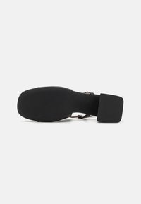 Sandale noire à talons blocs avec une semelle en caoutchouc lisse et de fines brides autour de la cheville. Présente un design polyvalent adapté à diverses occasions.