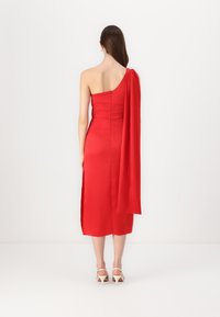 Robe en satin rouge avec une bretelle unique et un accent de tissu fluide ; longueur genoux avec une fente sur le côté pour le mouvement, mettant en valeur une silhouette ajustée.