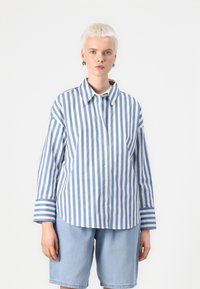 Striped button-up shirt in light blue and white cotton, featuring a collar, long sleeves, and cuffs with narrow stripes. Paired with denim shorts.
