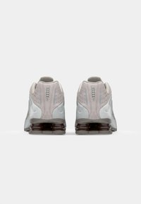 Des chaussures de sport gris clair et rose avec une tige en suède texturé, des détails en mesh et une semelle translucide sombre, dotées d'un design de talon rembourré.