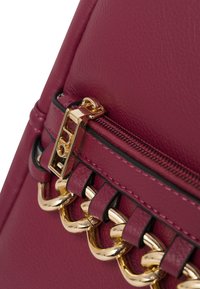 Borsa in pelle bordeaux con chiusura zip, hardware tono oro e dettagli decorativi con catene dorate lungo la cucitura.