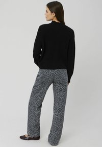 Pull en tricot noir à col montant, associé à un pantalon large gris avec un imprimé léopard noir. Des chaussures sombres complètent la tenue.