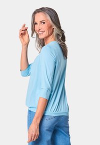 Helles Blau, Oberteil mit drei Viertelärmeln, runder Ausschnitt und elastischem Bund. Tragen mit Denim-Jeans. Weicher, glatter Stoff.