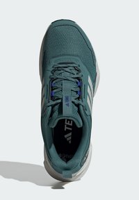 Teal sportsko med mesh-struktur, hvide accenter og blå snørebånd. Har en polstret krave og en tekstureret sål for greb og komfort.