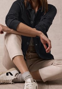 Sort knapjakke med en afslappet pasform, parret med beige cropped bukser. Fodtøj inkluderer hvide sneakers med sorte detaljer.