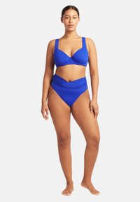 Niebieski zestaw bikini z usztywnionym stanikiem na szerokich ramiączkach i wysoko wciętą dolną częścią z zawiązanym wzorem, wykonany z gładkiego materiału.