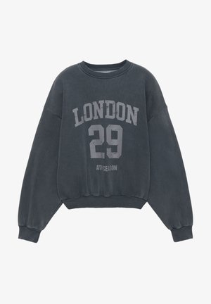 Tamnosiva dukserica okruglog izreza, s padnutim ramenima i rebrastim manšetama. Na prednjoj strani otisnuti natpisi "LONDON" i "29".