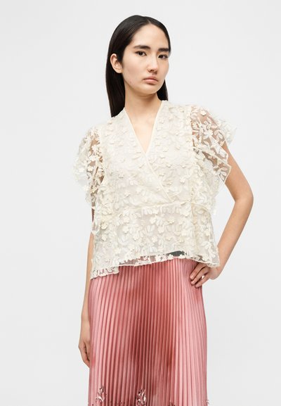 Haut transparent ivoire avec superposition en dentelle florale, décolleté en V et manches à volants, associé à une jupe plissée rose pastel.