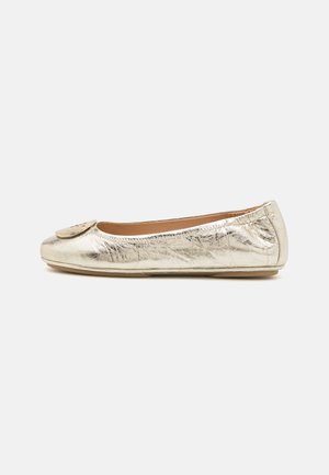 Metallic kuldne ballet-lame, millel on sile, läikiv tekstuur, ümar varvas ja dekoratiivne ringikujuline aksessuaar ülaosas.