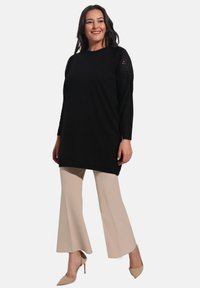 Black knitted tunic with long sleeves featuring a textured design. Paired with beige flared pants and nude high heels.