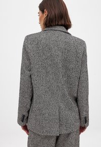 Textured black and white herringbone blazer with a single vent, notched lapels, and buttoned cuffs, showcasing a tailored fit.