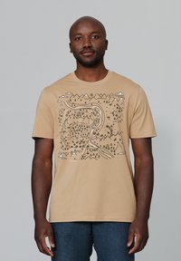 Bruine katoenen t-shirt met een zwart grafisch ontwerp van bergen, bomen en een kronkelige rivier, verrijkt met accenten van wolken en zon.