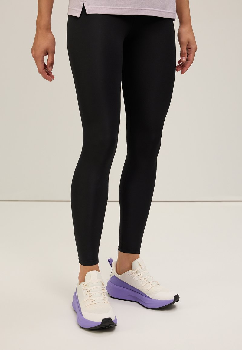 Zwarte leggings met een gladde, rekbare textuur, gecombineerd met witte en paarse sport schoenen met een chunky zool en mesh accenten.