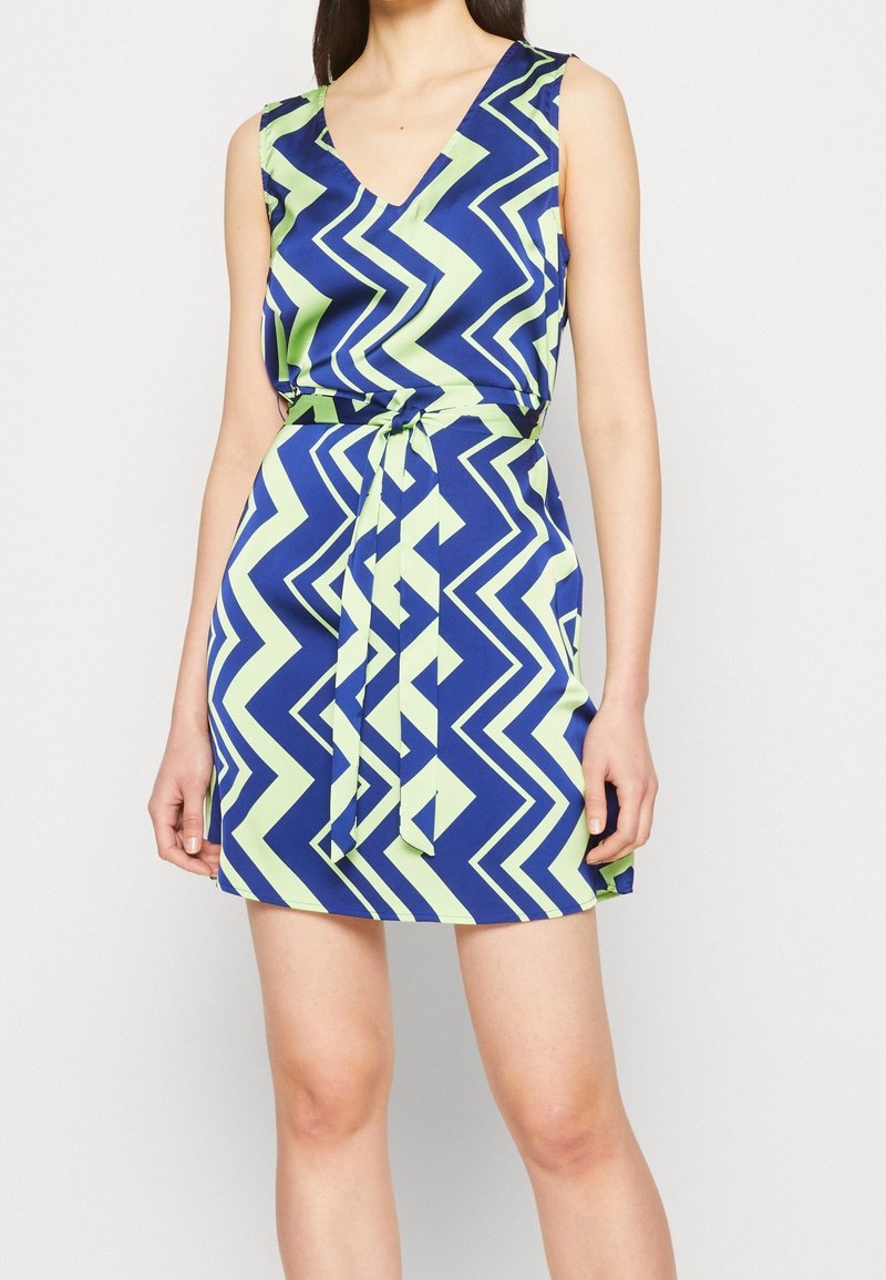 Bezrukávové šaty v modro-zeleném zigzag vzoru, s hlubokým výstřihem do V a látkovým páskem v pase pro vypasovaný siluetu.