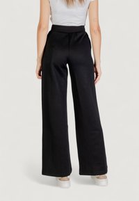 Pantalones anchos negros con un patrón texturizado, cintura elástica y tejido suave. Combinados con zapatillas blancas para un look casual.