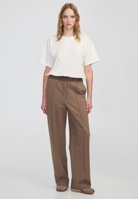 Biała koszulka z krótkim rękawem w luźnym fasonie, zestawiona z brązowymi spodniami o szerokich nogawkach, z elastycznym paskiem i detalem sznurkowym.