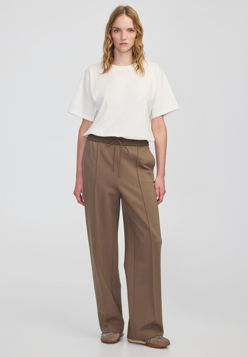 Biała koszulka z krótkim rękawem w luźnym fasonie, zestawiona z brązowymi spodniami o szerokich nogawkach, z elastycznym paskiem i detalem sznurkowym.
