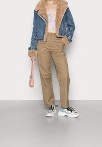 Chaqueta de mezclilla con forro de piel sintética, pantalones cargo beige y zapatillas blancas con detalles azules. Un pequeño bolso rosa completa el atuendo.