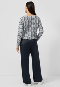 Hellblauer und cremefarbener gestreifter Pullover mit Wellenmuster, kombiniert mit dunkelblauen, weit geschnittenen Hosen und weißen Sneakern.