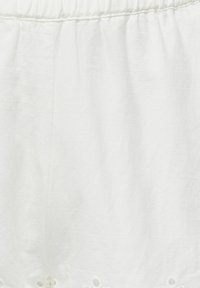 Witte linnen kledingstuk met een gestructureerde afwerking, voorzien van een geplooide tailleband en perforaties langs de zoom.