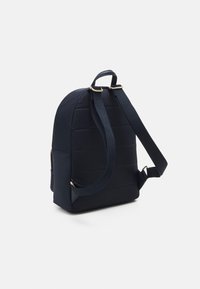 Mörkblå ryggsäck med justerbara remmar, vadderad baksida och sidoficka med dragkedja mot vit bakgrund.