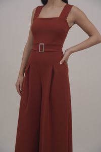 Lange jumpsuit in roestkleurige stof, met een vierkante halslijn, verstelbare banden en een vlakke tailleband met een zilveren rechthoekige gesp.