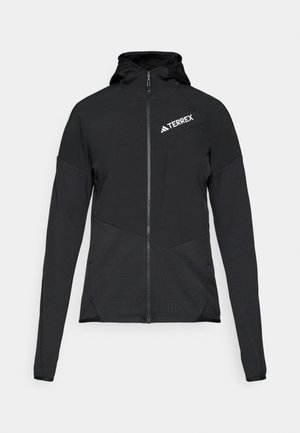Čierna bunda Terrex so zipsom vpredu a kapucňou. Má štruktúrovanú látku, priliehavé rukávy a logo na ľavej hrudi.