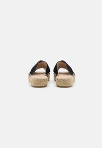 Crni suède espadrile na slip-on s otvorenom stražnjom stranom i pletenom jute potplatom, sa glatkom unutarnjom podlogom i minimalnim dekorativnim detaljima.
