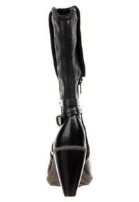 Musta nilkkasaapas, jossa on teksturoitu kangasvarsi ja kiiltävät nahkayksityiskohdat. Ominaisuuksiin kuuluu matala, kapeneva korko ja säädettävä nilkkahihna.